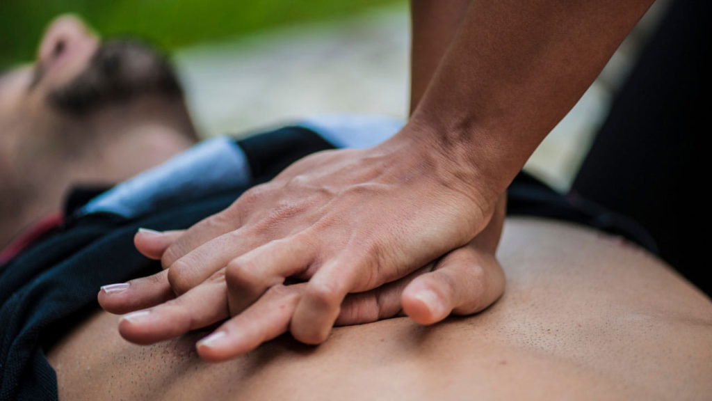 A person performing CPR with both hands pressing on another person's chest. The background is blurred, highlighting the focus on the hands and chest area.