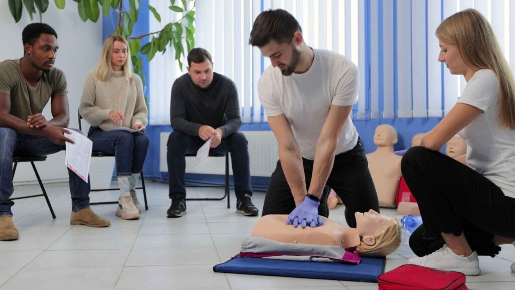 CPR course with a student performing CPR technique on a mannequin and other students and instructor overseeing