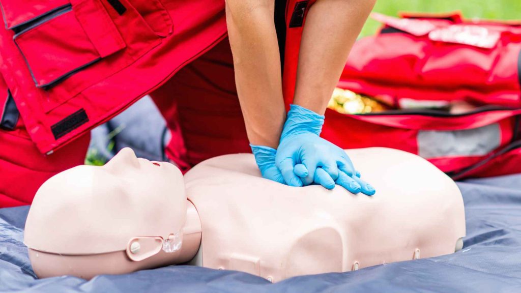 close up of a person wearing nitrile gloves and performing cpr on a manikin outside