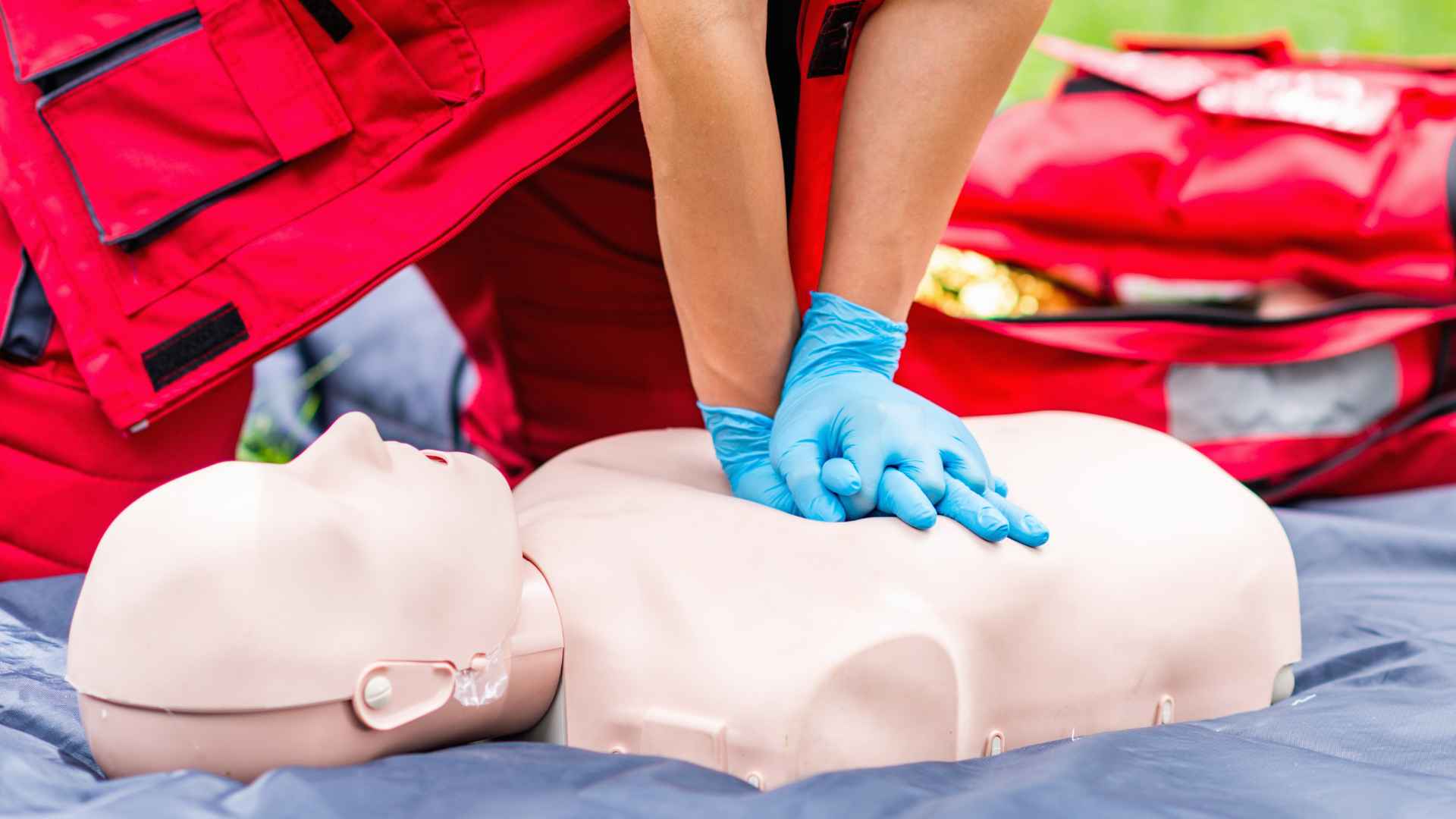 close up of a person wearing nitrile gloves and performing cpr on a manikin outside