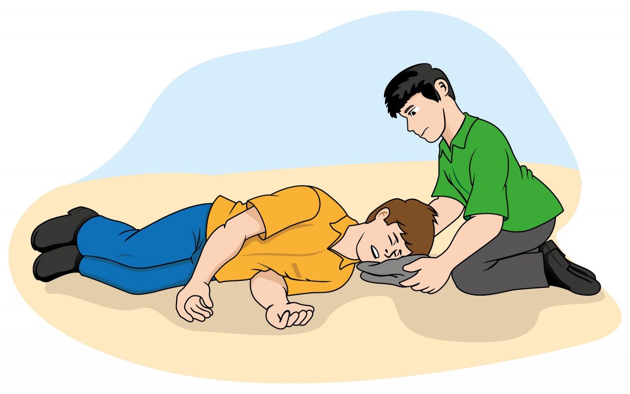Illustration of a person in a green shirt assisting another person in an orange shirt, who is lying on the ground in the recovery position after an seizure episode. The helper gently supports the person's head with a cushion.