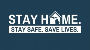 Text on a dark blue background reads "STAY HOME. STAY SAFE. SAVE LIVES." The word "HOME" features an image of a house with a silhouette of the state of Michigan inside the letter "O.