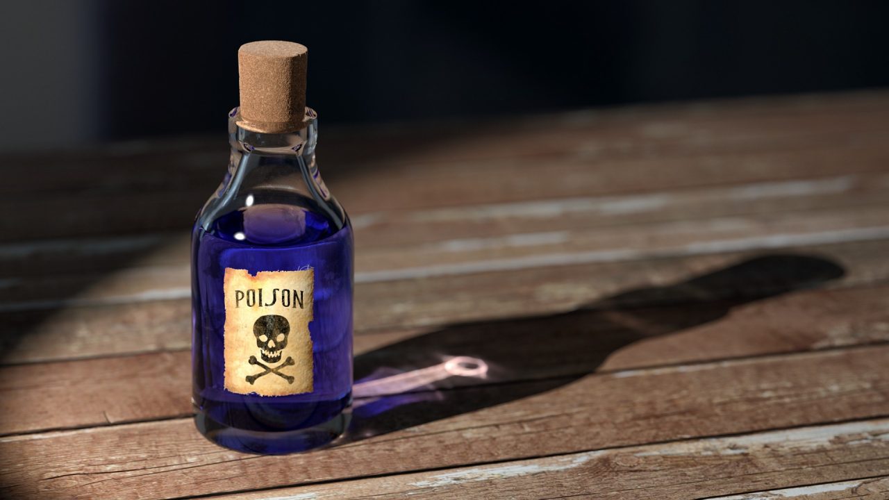 A small glass bottle with a cork stopper, filled with blue liquid. It has a label with a skull and crossbones and the word "POISON." The bottle casts a shadow on a wooden surface.