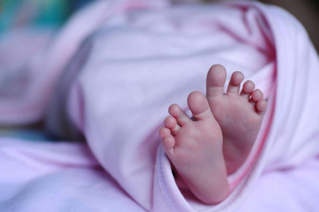 Close-up of a baby's feet peeking out from a soft, light pink blanket. The blanket is wrapped snugly around the baby, creating a cozy and warm scene.