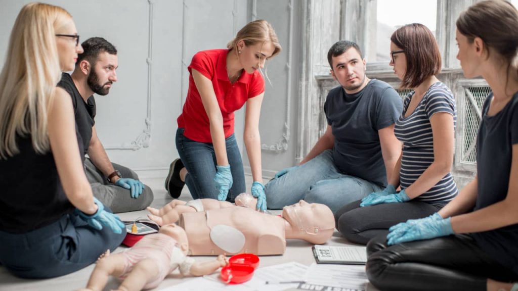 a group of people gather around a mannequin in a CPR course