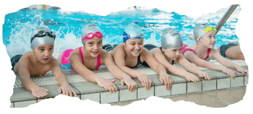 Five children wearing swim caps and goggles smiling and leaning over the edge of a swimming pool. They appear to be preparing or learning to swim, with water splashing in the background.