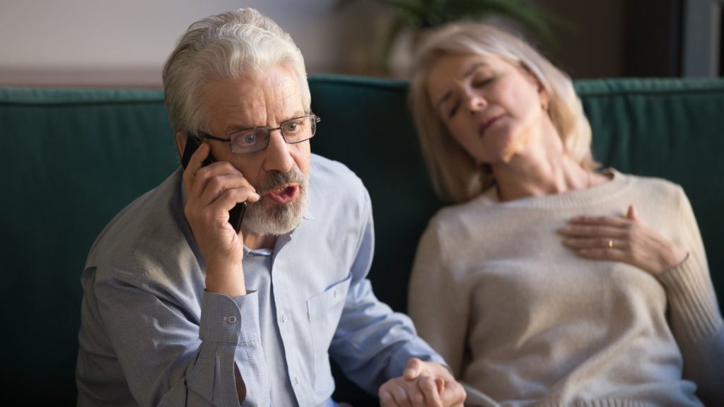 A man urgently calling 911 as his wife experiences chest pain, possibly indicating a heart attack