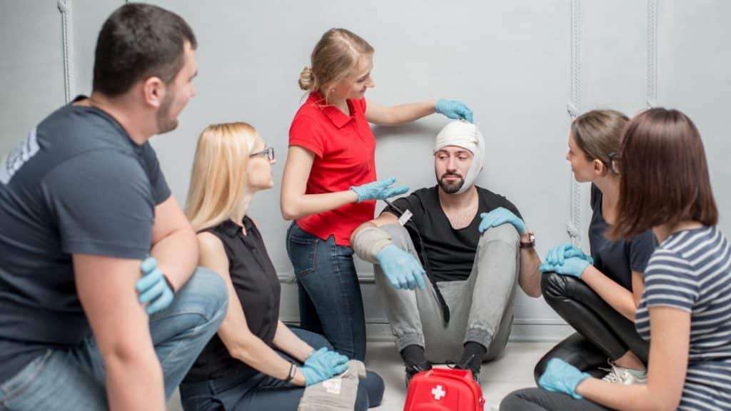 A woman demonstrating first aid techniques by gently touching someone's head while explaining to a group during a first aid course.