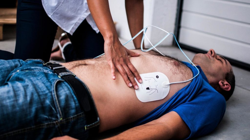Person using an AED device during CPR on a patient, demonstrating emergency response for cardiac arrest.