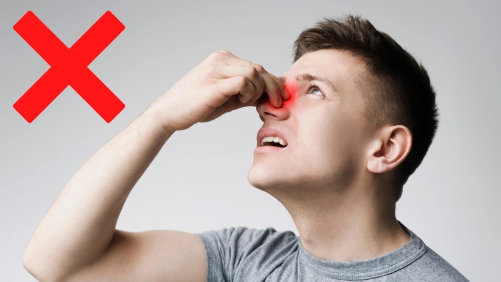 A person pinches the bridge of their nose with a red spot highlighting the area, suggesting sinus discomfort. A red "X" is in the upper left corner, indicating a negative or incorrect action. The background is plain gray.
