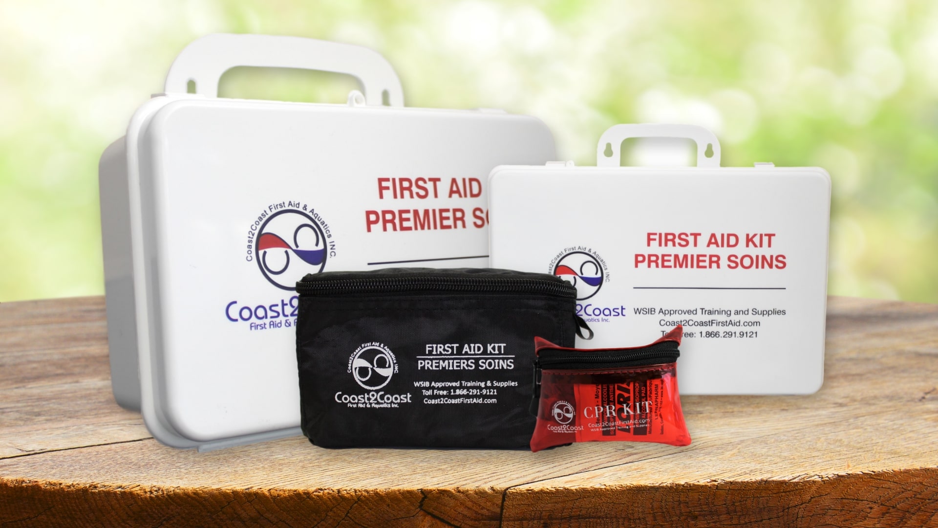 Four Coast First Aid Kits of different sizes are displayed on a wooden surface outdoors. The kits, in white, black, and red cases, are labeled "FIRST AID KIT PREMIER SOINS." Green foliage is blurred in the background.
