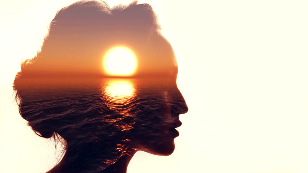A silhouette of a woman's profile is overlaid with an image of a sunset over the ocean. The sun appears as a bright orb near her forehead, casting warm hues across her face and creating a double exposure effect.