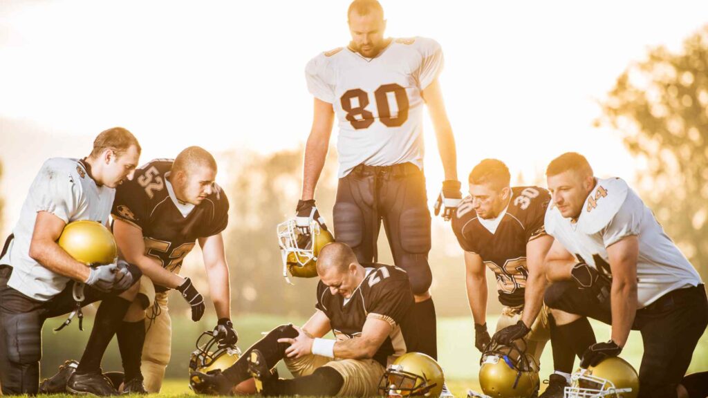 A group of soccer players in the field with one of them injured with sprain in the leg.