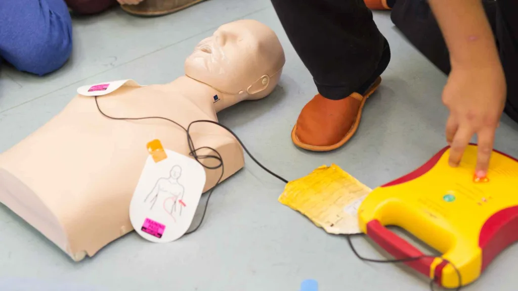 person practicing using an aed on a cpr manikin. the person is pressing the "deliver shock" button on the training aed