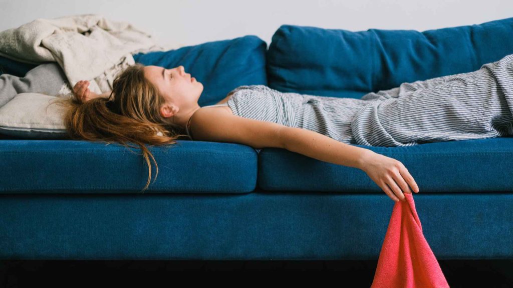 woman laying flat on a blue couch looking up at the ceiling