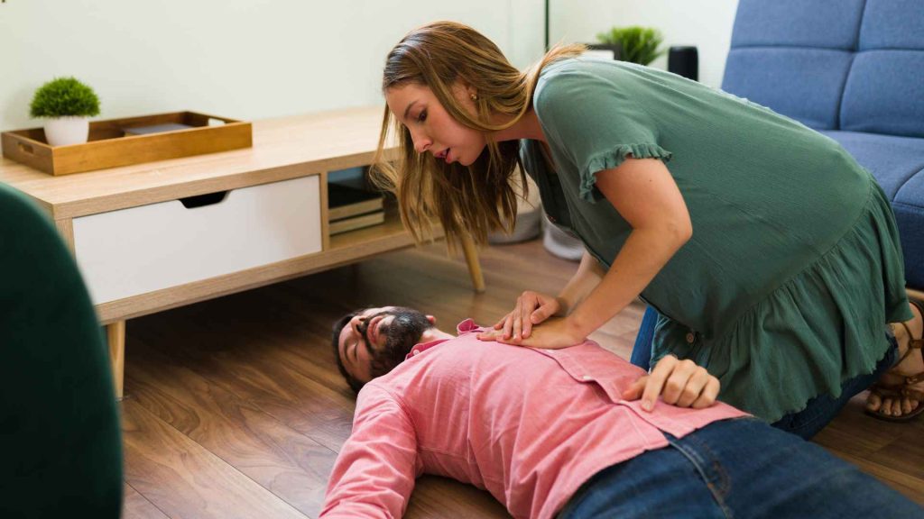woman checking on a man who is laying on the ground in a living room or break room unconscious