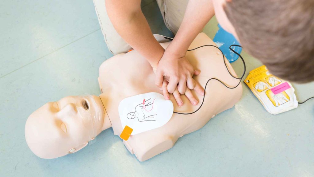 top view of a person doing compressions on a cpr manikin that has aed pads on the chest