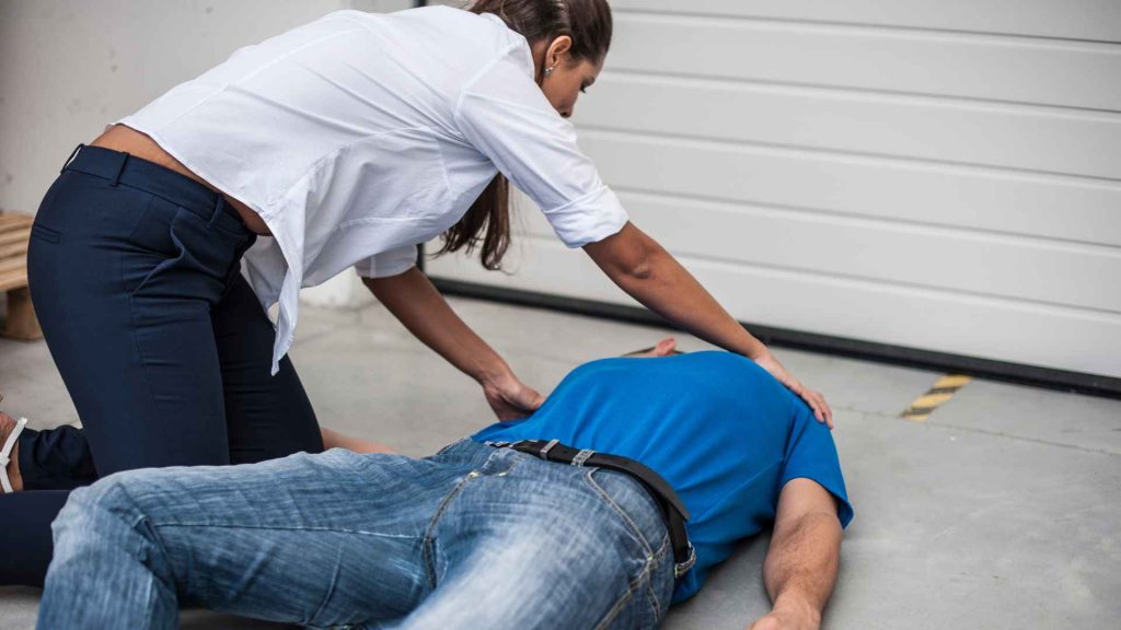 woman checking on a man who has fallen unconscious on the floor.