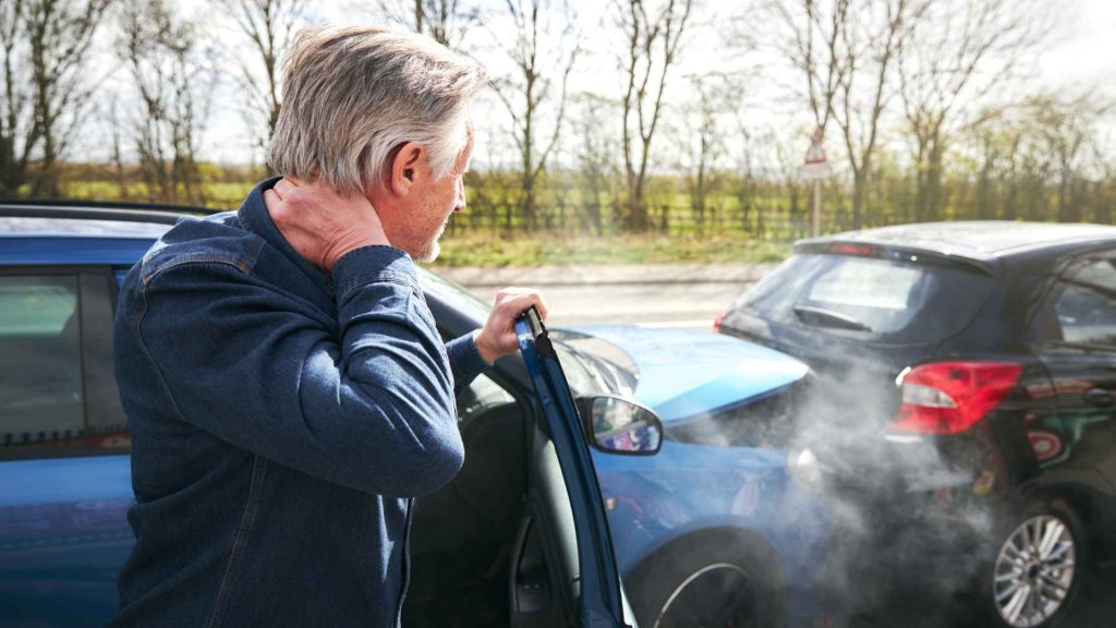 man stepping out of a car holding his neck after a car accident