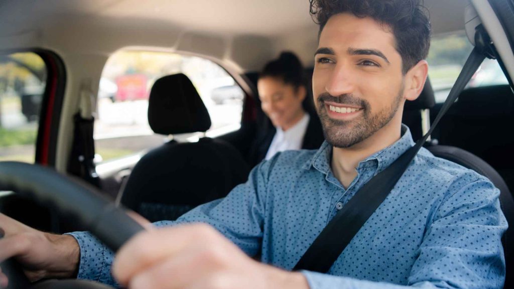 close up of a man in a blue dress shirt driving a woman who is sitting in the back seat