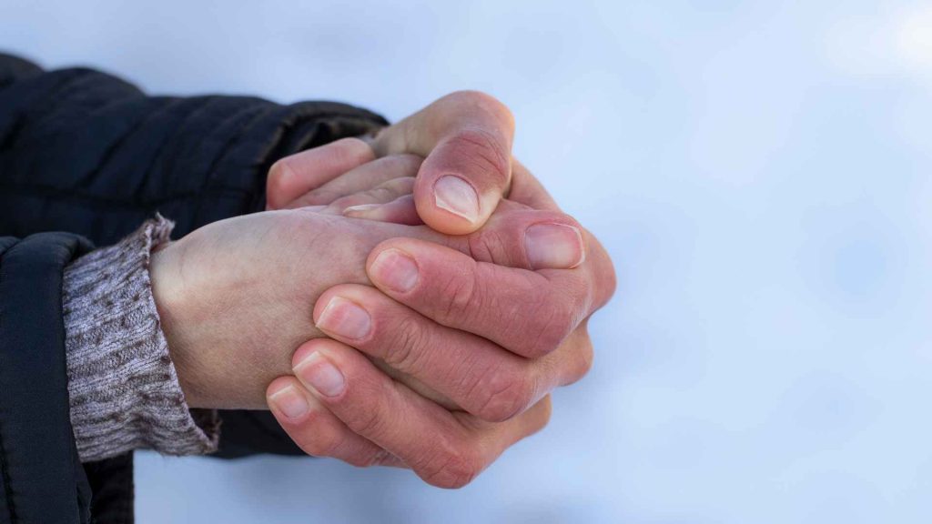 close up of a person's hands together in front of snow. the fingers are turning pink due to oncoming frostbite