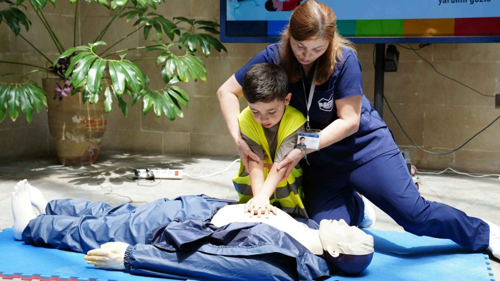 woman teaching a young child how to perform cpr compressions on a manikin