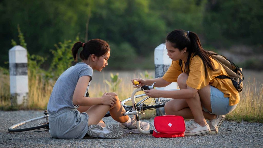 a teenage girl performing first aid on another teenage girl who fell off her bike. 