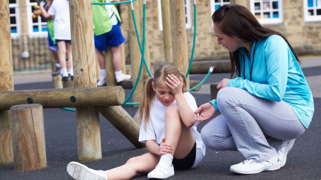 female adult assisting female child after an injury on a playground. child is holding her head and leg