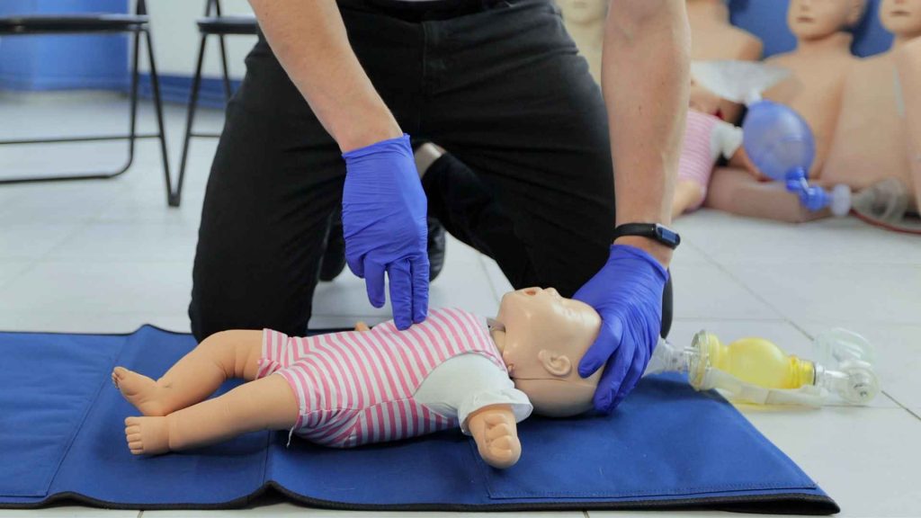 close up of a man doing cpr on an infant manikin